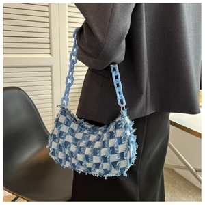 Detail van blauwe denim schoudertas met dambordpatroon, gerafelde randen en grove plastic ketting