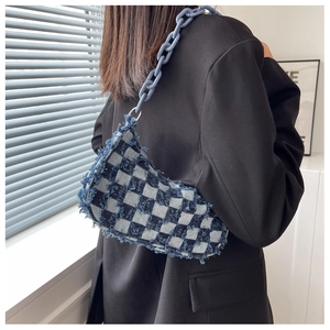 Detail van blauwe denim schoudertas met ruitpatroon, franjes en lichtblauwe ketting