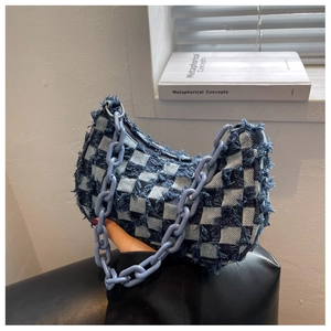 Detail van geblokte denim schoudertas met onafgewerkte randen en een dikke blauwe ketting