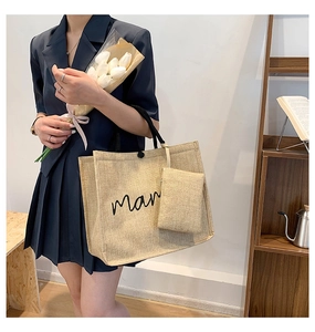 Detail of beige linen tote bag with black handles and small zipper pouch attachment