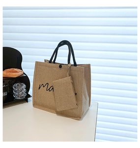 Detail of jute tote bag set with black rope handles and cursive text on a white background