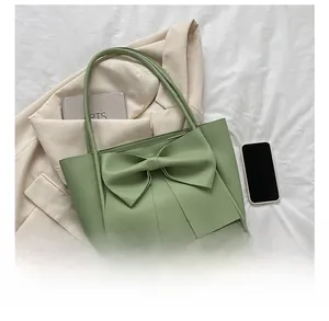 Sac fourre-tout vert avec grand nœud et bandoulière à côté d'un smartphone