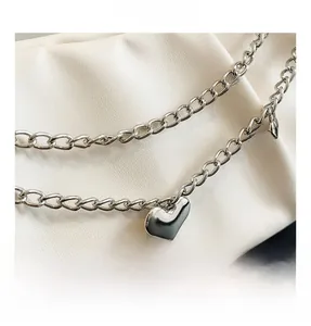 Detail of silver heart charm and polished chain hardware on white pleated leather handbag