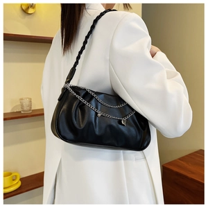 Detail of black pleated underarm bag with silver chain and heart pendant on white blazer