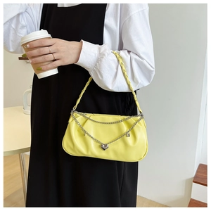 Detail of bright yellow baguette bag with silver heart chain and woven shoulder strap