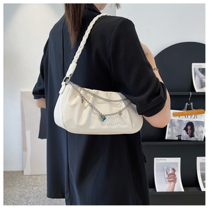Detail of white pleated cloud bag with braided strap and heart pendant on metal chain