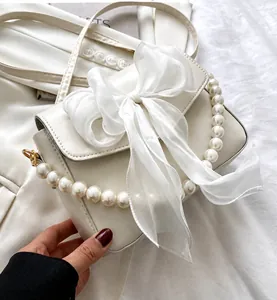 Detalle de bolso blanco con lazo de organza y correa de cadena de perlas