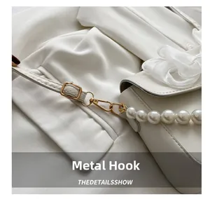 Detail of white leather shoulder bag featuring gold metal hooks and pearl chain strap