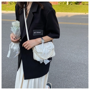 Detail of white PU bag featuring large organza bow and pearl handle in natural light
