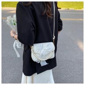 White shoulder bag featuring a large mesh bow and elegant pearl chain accessory