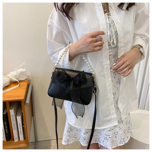 Close-up of black crossbody bag featuring a large organza bow and pearl chain handle