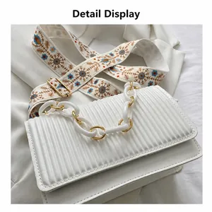 Detail of white pleated handbag with acrylic chain handle and floral embroidery strap