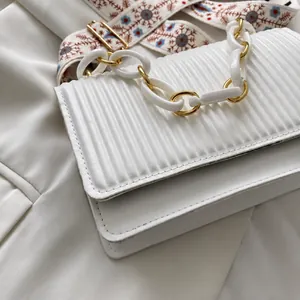 Close-up of white pleated crossbody bag with gold chain and bohemian embroidered strap