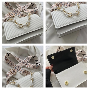 Detail of white pleated shoulder bag featuring floral embroidery strap and gold chain link