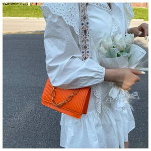 Detail of vibrant orange shoulder bag with vertical pleats and amber chain decoration