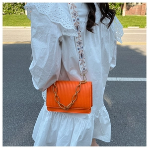 Detail of orange accordion pleat bag with amber chain and floral embroidered strap