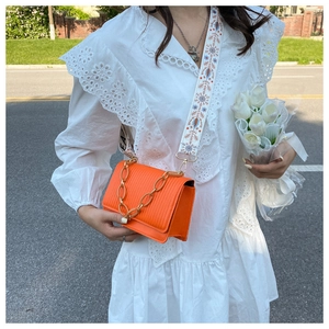 Detail of orange crossbody bag with gold chain and floral embroidered strap