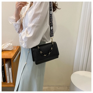 Detail of black pleated shoulder bag with embroidered strap and decorative chain