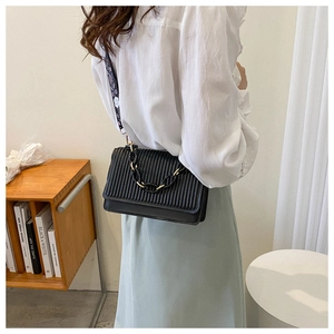 Detail of black pleated leather shoulder bag with chain and geometric patterned strap