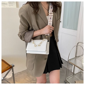 White pleated crossbody bag with a colorful ethnic embroidery strap on olive blazer