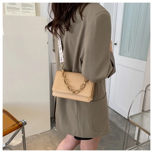 Detail of khaki pleated crossbody bag with gold chain and embroidered strap on model