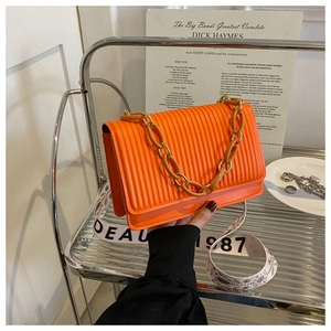 Detail of orange pleated crossbody bag featuring metal chain and wide floral strap