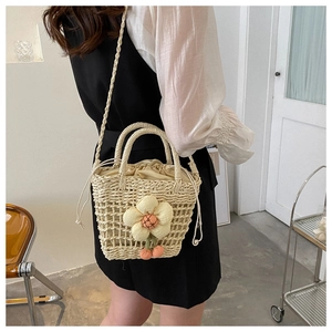 Detail of straw bucket bag with floral appliqué and woven strap in beige white