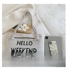 Detail of canvas tote bag with HELLO WEEKEND slogan, rope handles and tassel accent