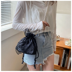 Detail view of black pleated bucket bag with pearl strap and drawstring closure