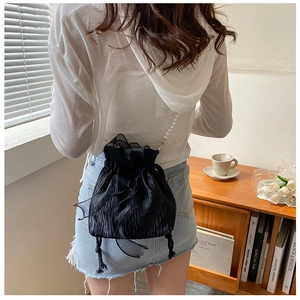 Detail of a black pleated bucket bag featuring a delicate pearl crossbody strap