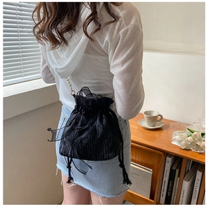 Detail of black drawstring bucket bag with large bow and pearl shoulder strap on model