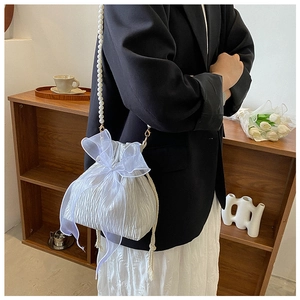 Close-up of white pleated bucket bag featuring pearl strap and organza bow detail