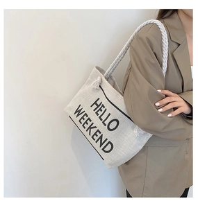 Detail of canvas tote bag with HELLO WEEKEND print and white rope straps on model