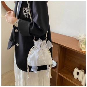 Detail of white pleated bucket bag with organza bow and pearl beaded shoulder strap