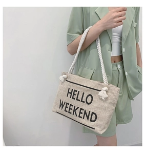 Detail of beige canvas tote with HELLO WEEKEND text and braided rope handles with tassels