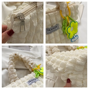Detail view of cream bubble puff handbag with zipper and floral charm accessory