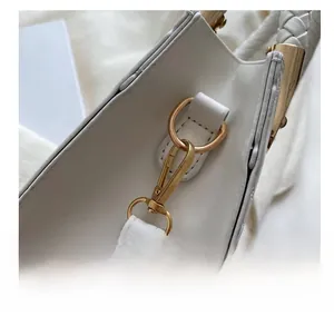 Close-up of golden metal hook on white litchi pattern leather handbag with fine stitching