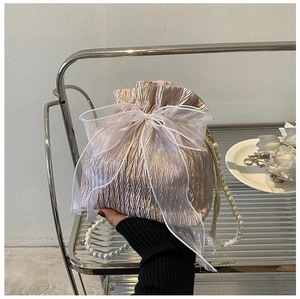 Detail of champagne pleated bucket bag with organza bow and pearl handle on a metal cart
