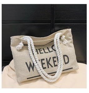 Detail of HELLO WEEKEND text on a natural straw tote bag with braided rope handles