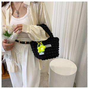 Detail of black bubble textured tote bag featuring fashion label and green floral charm