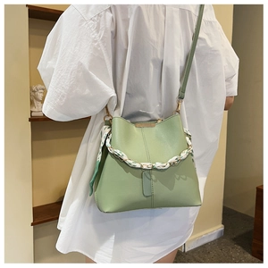 Detail of light green bucket bag featuring a silk scarf-wrapped chain strap and metal hardware