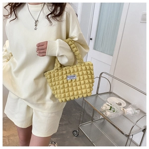 Detail of yellow bubble textured handbag with Fashion Instinct label held by a model