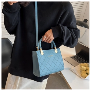 Detail of light blue quilted handbag with woven handle and gold hardware in lifestyle setting