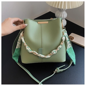 Close-up of green bucket bag with gold chain handle wrapped in silk scarf