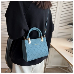 Detail of light blue quilted handbag featuring a unique woven handle and fashion text