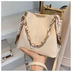 Detail of cream bucket bag featuring a silk scarf handle and light gold metal chain link