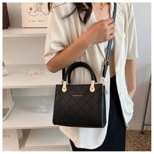 Detail of black quilted handbag with woven round handle and golden metal hardware