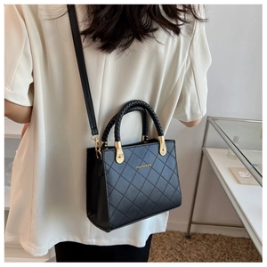 Detail of black quilted crossbody bag with woven handle and gold hardware shown on model