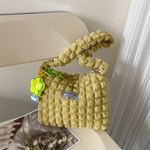 Sac à bandoulière moutarde plissé avec breloque fleurie sur une chaise blanche