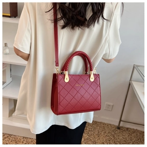 Detail of red quilted handbag with woven handle and gold hardware shown on model